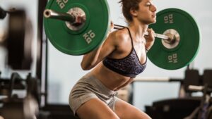Muscular build sportswoman exercising with barbell in a squat position.