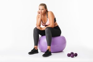 young-woman-with-excess-weight-sporty-top-leggings-sitting-fitness-ball-with-dumbbells-near-thoughtfully-looking-camera-white-background-isolated.jpg