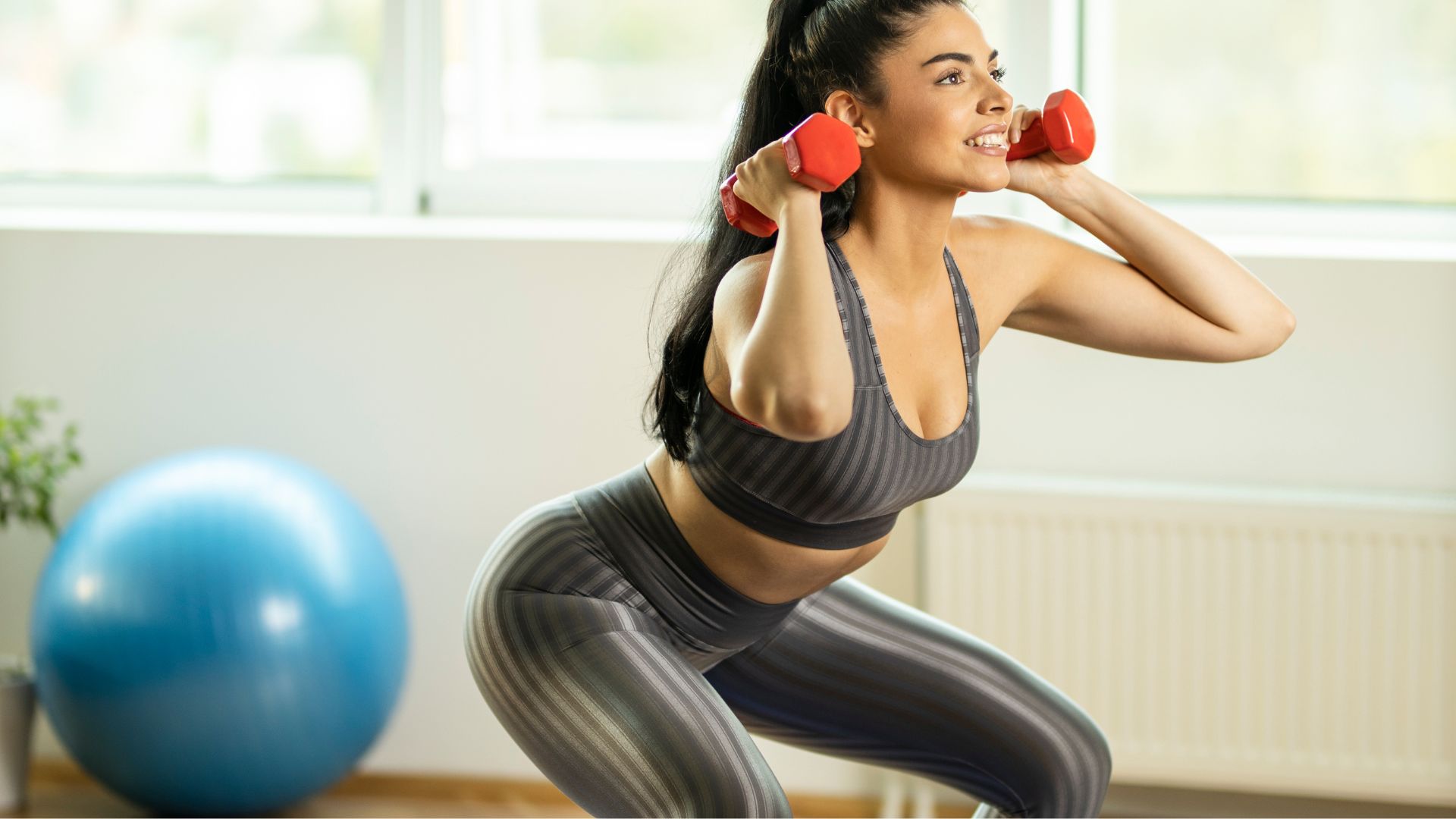 Fit woman doing squats with dumbbells at home