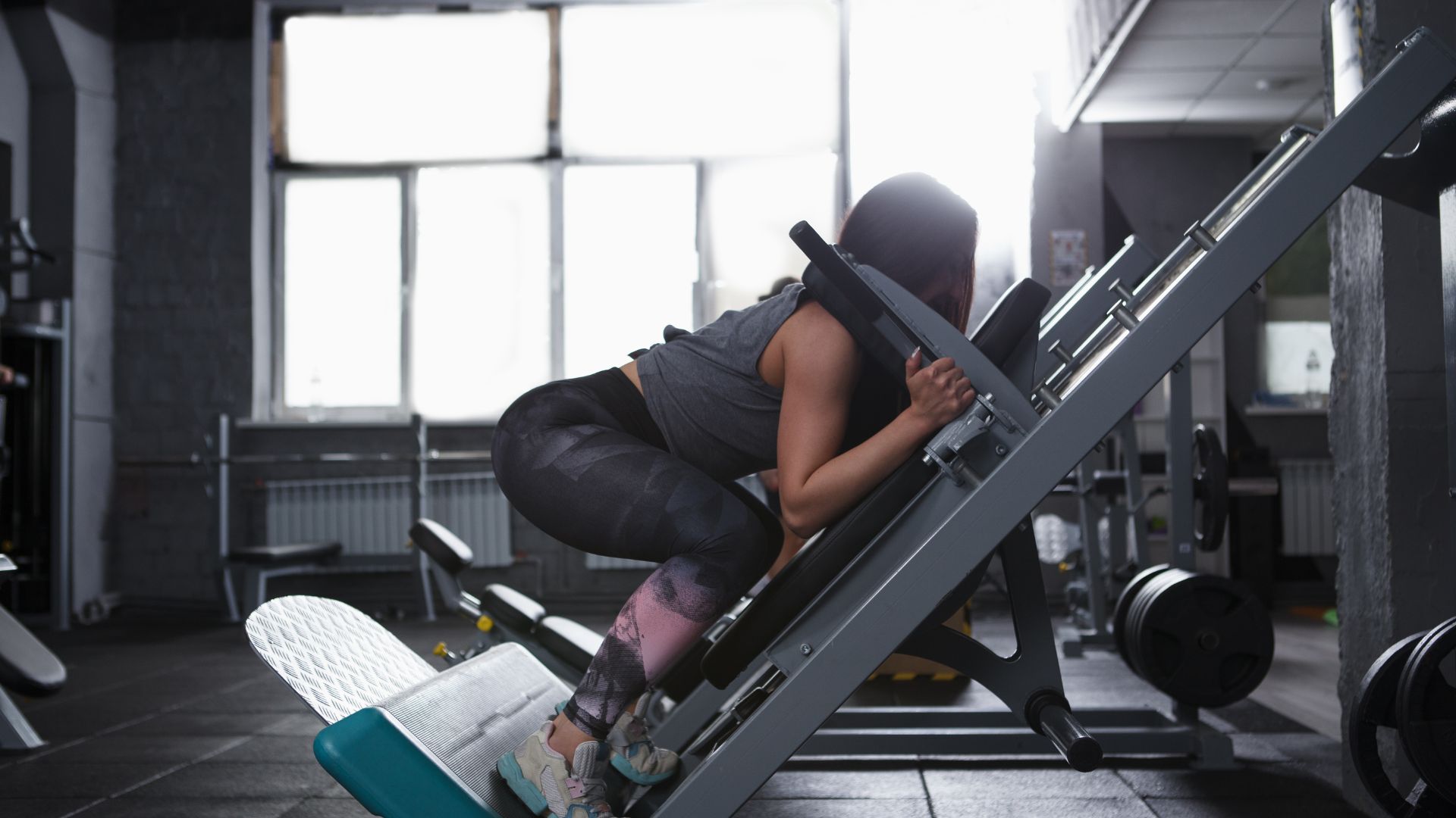 Profile shot of a strong athletic woman doing squats in hack squat gym machine